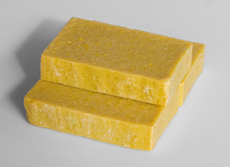 Tres barras de jabón artesanal de color amarillo claro y textura gruesa apiladas horizontalmente.