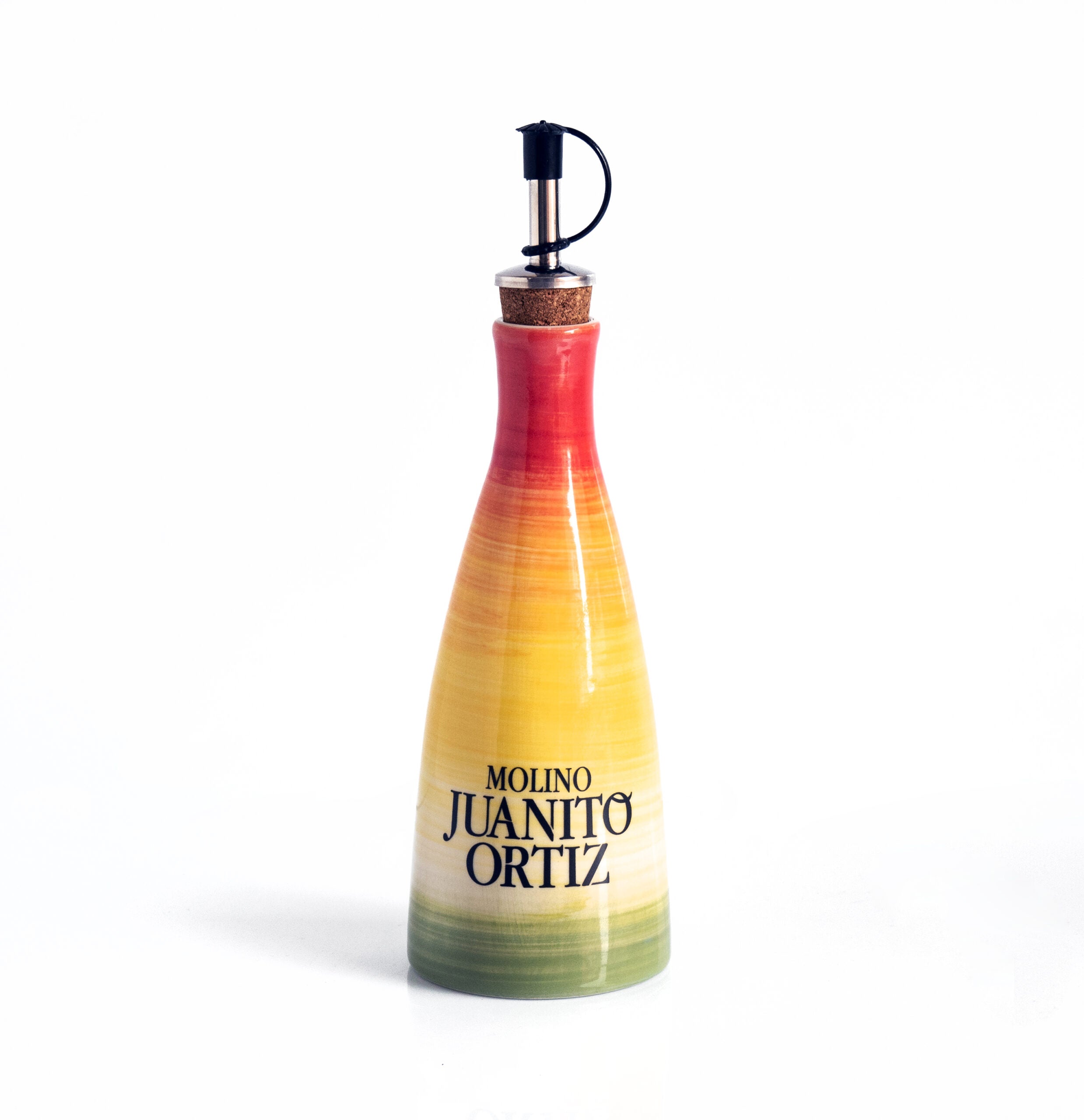 Una aceitera de cerámica, alargada y de cuello estrecho, con un tapón de corcho y un dosificador metálico. La aceitera tiene un diseño pintado con franjas degradadas en tonos rojos, anaranjados, amarillos y verdes, con el logotipo "Molino Juanito Ortiz" en negro. El fondo es liso y de color claro.