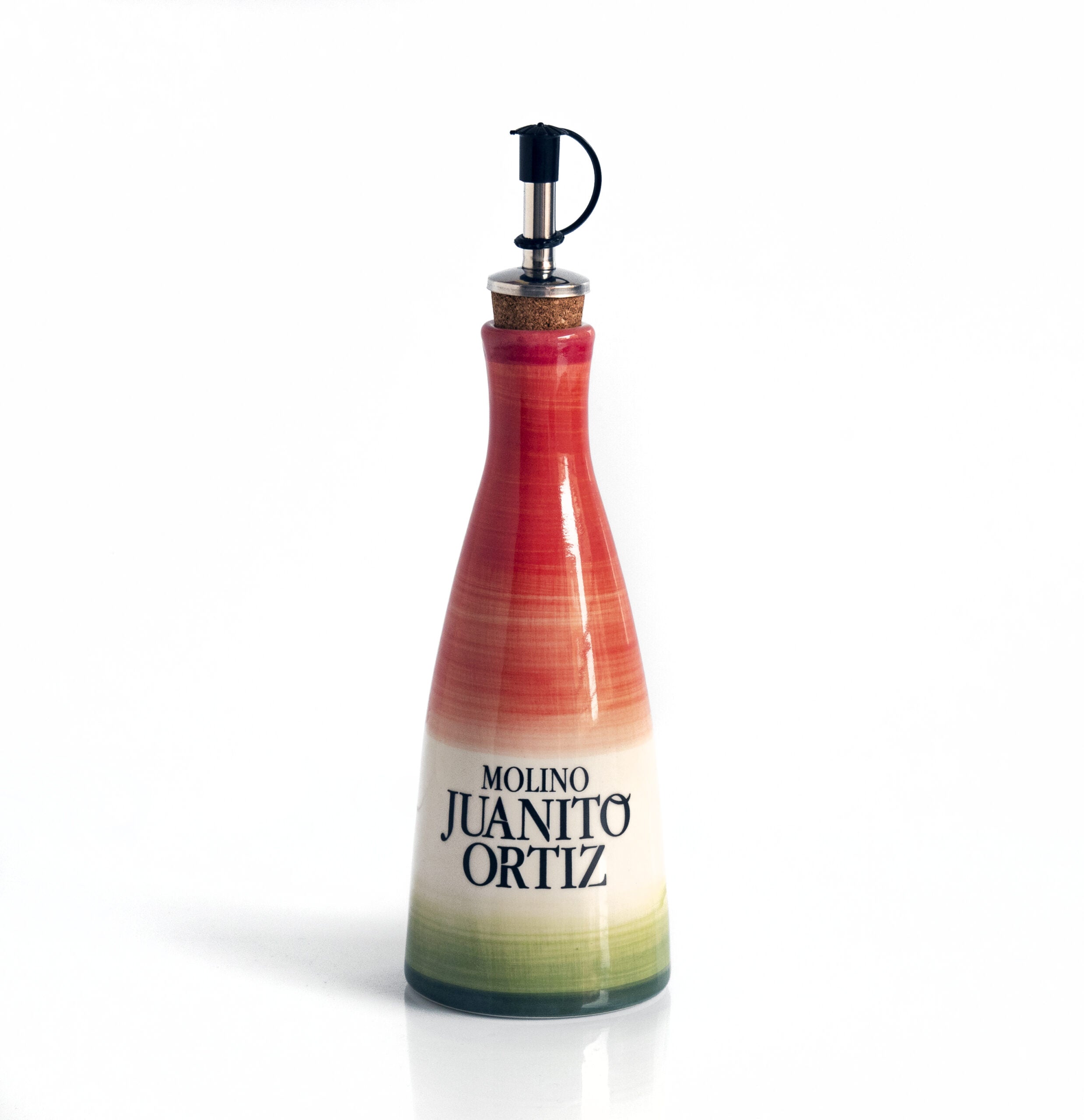 Una aceitera de cerámica, alargada y de cuello estrecho, con un tapón de corcho y un dosificador metálico. La aceitera tiene un diseño pintado con franjas degradadas en tonos rojos, rosados y verdes, con el logotipo "Molino Juanito Ortiz" en negro. El fondo es liso y de color claro.