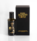 Una botella de vidrio oscura de 250 ml de aceite de oliva "Molino Juanito Ortiz" con un diseño dorado de un hombre sentado con un perro, junto a una elegante caja negra con letras doradas.